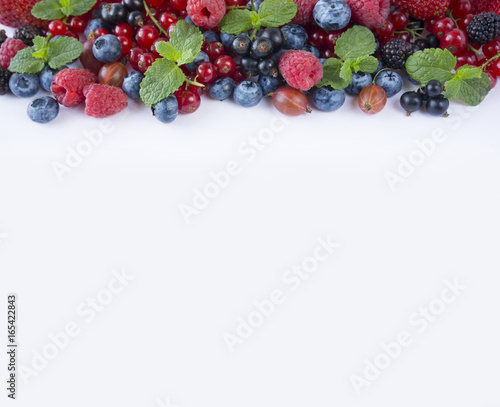 Various fresh summer berries on white background. Ripe blueberries, raspberries, gooseberries, red and black currants. Berries at border of image with copy space for text.