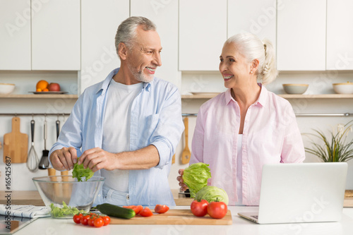 Mature loving couple family using laptop and cooking salad