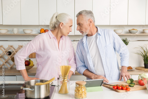 Angry mature man standing near mature serious woman at kitchen