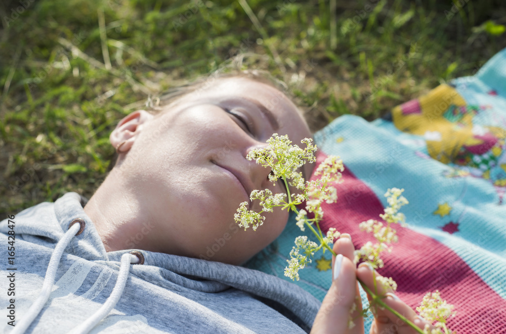 Obraz premium A young girl lies on the field and sniffs a flower