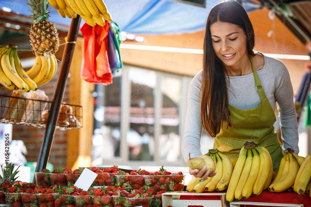 Obraz premium Young attractive fruit market saleswoman sells fresh fruit on the street market.