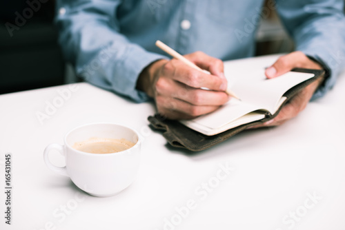 cropped view of male hands with coffee cup writing in diary © LIGHTFIELD STUDIOS