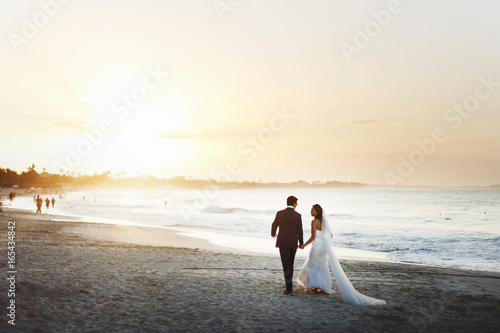 Bride and groom hold each other hands posing on the beach