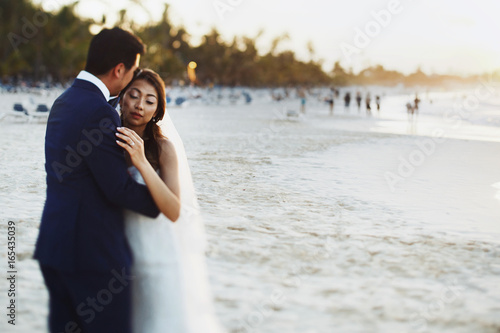 Bride and groom hug each other tender standing in the rays of golden sun on the beach