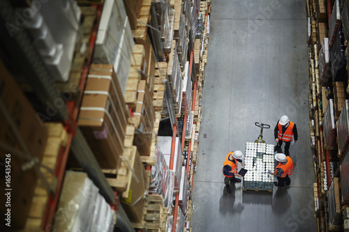 Above view of people working in large warehouse, counting goods on moving cart between shelves with packed boxes photo