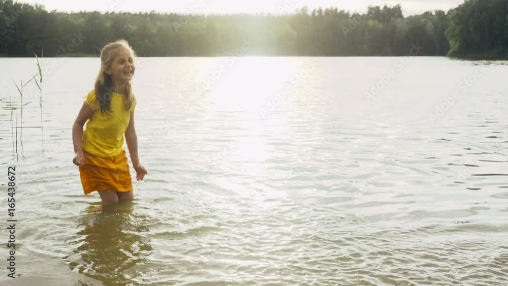 Little girl in yellow clothes splashing in the water of a forest lake. Slow motion.