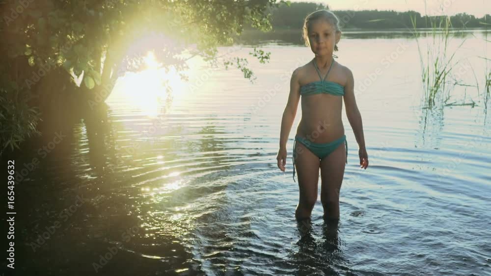 Cute little girl is splashes and catches soap bubbles standing in the water of a picturesque forest lake in the light of a glares on the water. Slow motion.
