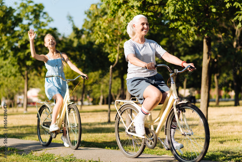 Obraz premium Cheerful senior woman riding bicycles with her granddaughter