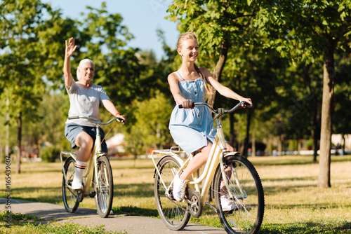 Positive teenager girl riding bicycles with her grandmother