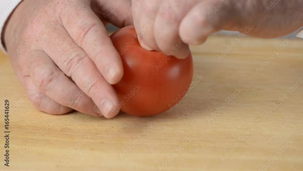 The man cuts juicy red tomato on slices by means of a big table knife The man cuts juicy red tomato on slices by means of a big table knife