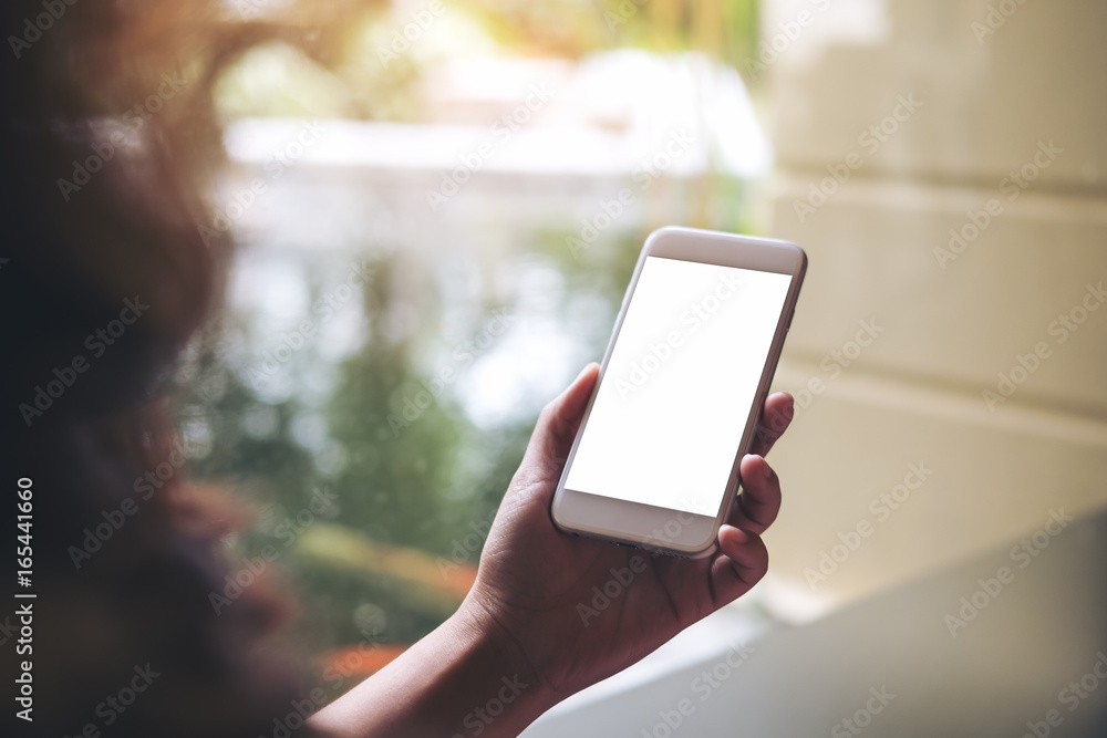 Mockup image of a woman holding and using white smart phone with blank screen with pond and nature background