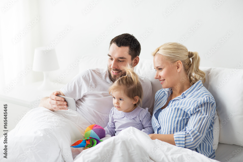 happy family with smartphone in bed at home