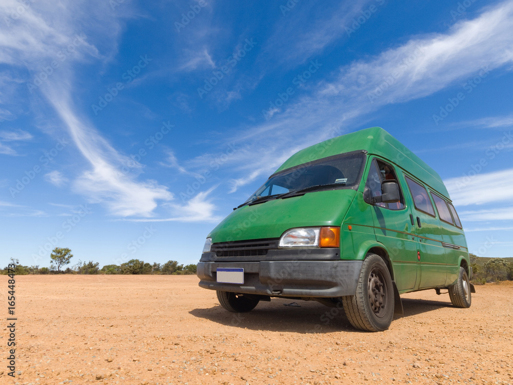 A old green backpackers motorhome camper van, in the Australian outback, with a vivid blue sky and famous red dirt floor. The Australian outback is a great place for travellers.