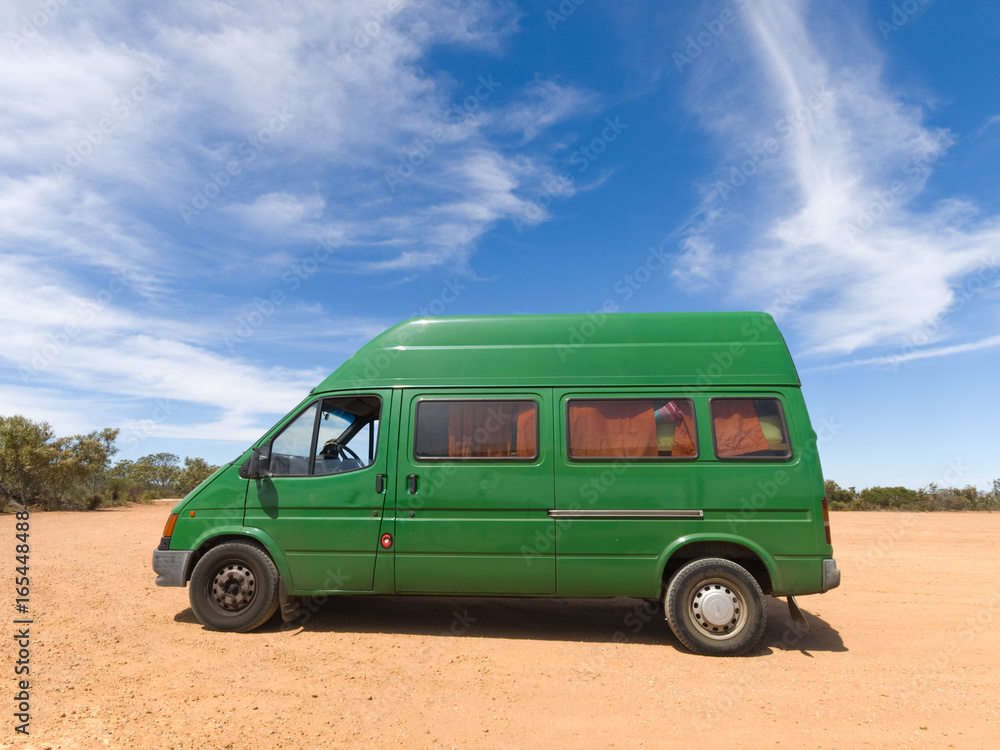 A old green backpackers motorhome camper van, in the Australian outback,  with a vivid blue sky and famous red dirt floor. The Australian outback is  a great place for travellers. Stock Photo