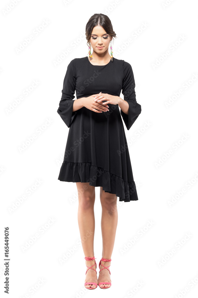 Classy elegant woman in black dress standing with clasped hands looking down. Full body length portrait isolated on white background. Classy elegant woman in black dress standing with clasped hands looking down. Full body length portrait isolated on white background.