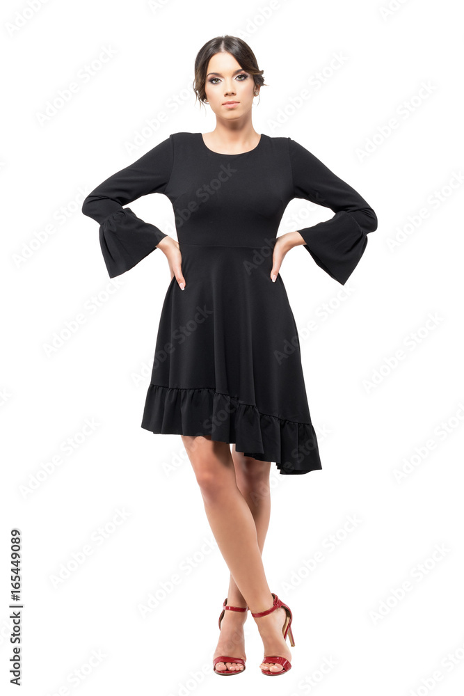 Charming Latin woman in black flounce dress standing and looking at camera with arms on hips. Full body length portrait isolated on white background. Charming Latin woman in black flounce dress standing and looking at camera with arms on hips. Full body length portrait isolated on white background.