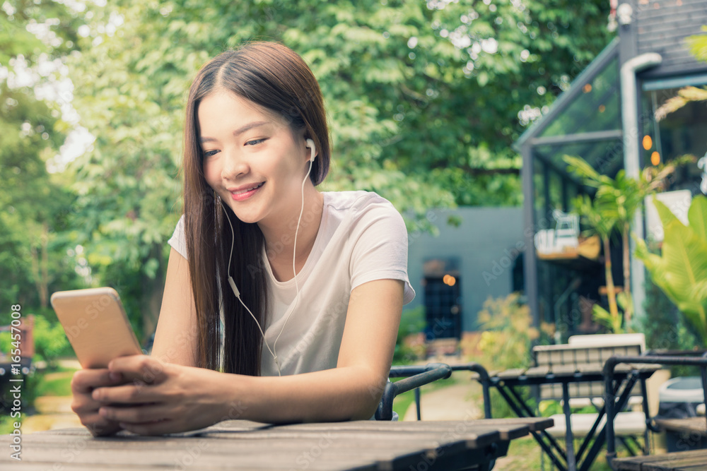 young happy woman in casual clothes sitting at an outdoor park listening to music on her phone, young happy woman in casual clothes sitting at an outdoor park listening to music on her phone,