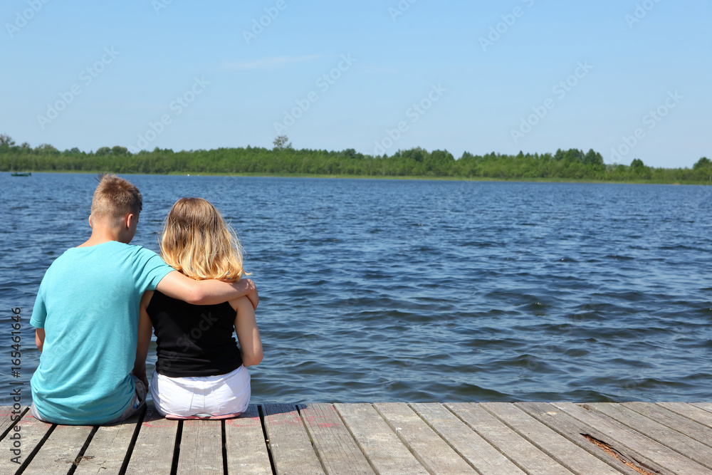 Teenagers on a lake date on a far-advanced jetty.
