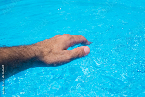 Male hand touching clear swimming pool water