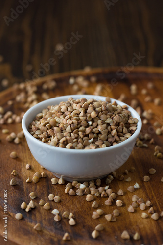 Buckwheat grain on ceramic bowl over wooden table.