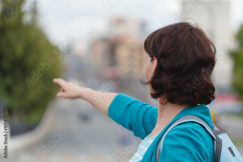 woman show left side hand show forefinger/index finger, correct, pointing, shoot, point up with blur building in the city background