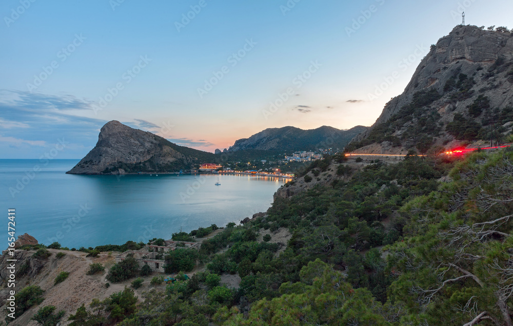 View of the Bay to the resort village near the mountains and with a large headland in the sea at sunset. Cape Chyken Peninsula of Crimea, resort Noviy Svet