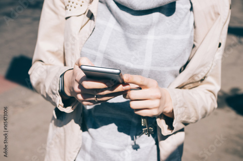 Young woman in a beige jacket holds a mobile phone