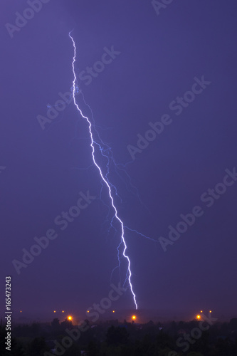 Single lightning in stormy sky over field and street lights