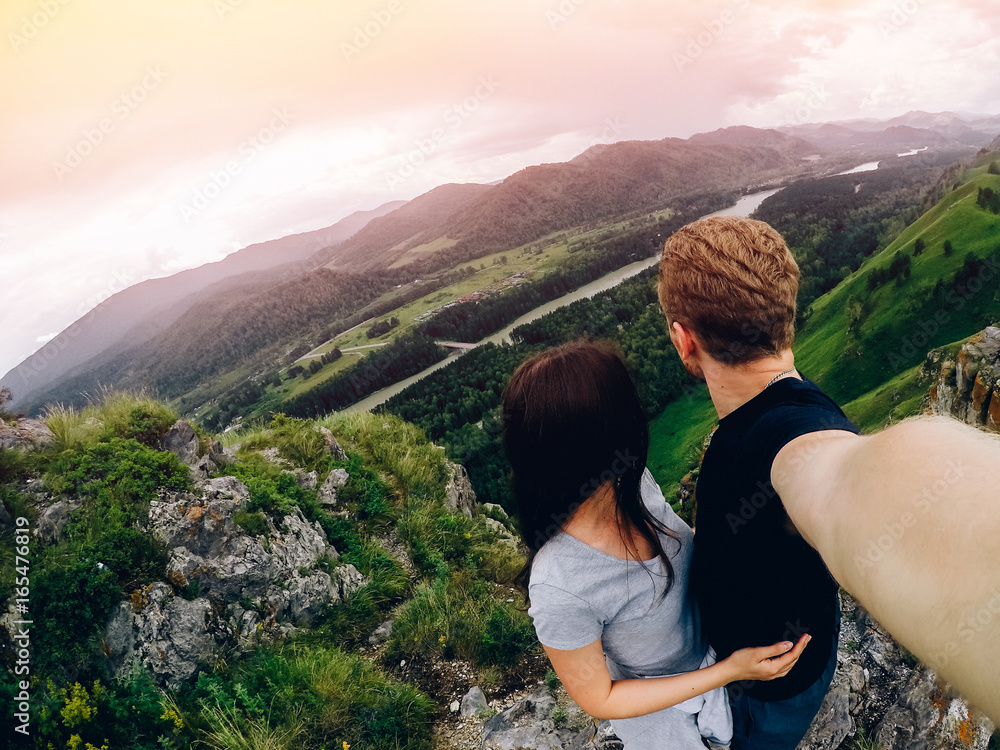 Naklejka premium Guy and girl tourists are happy, hug and do selfie on action camera on background of mountains, forests. Concept love and travel. Russia, Altai Mountains.
