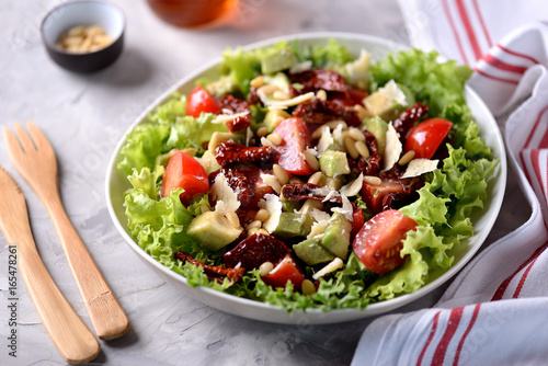 Salad from lettuce, cherry tomatoes, dried tomatoes, avocado, parmesan, pine nuts with olive oil. Healthy food.