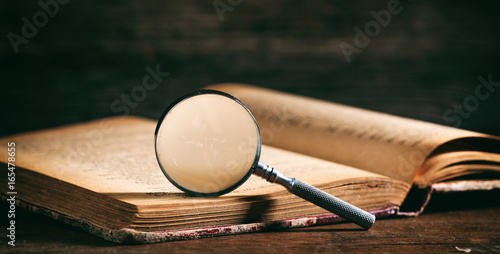 Vintage book and magnifying glass on wooden desk