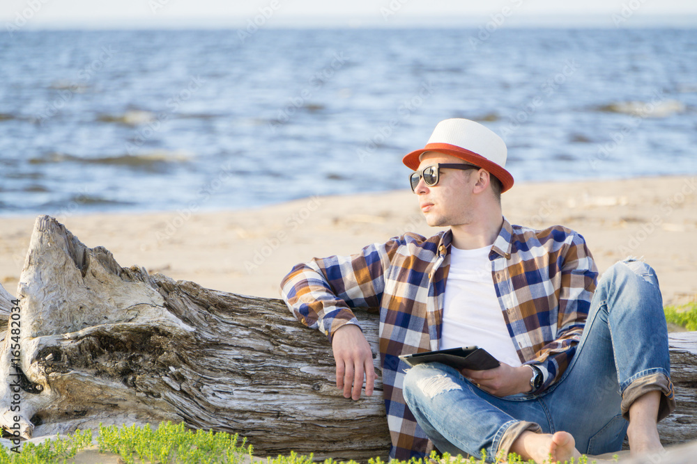 A man in smart casual hipster style with tablet combining work with relax on the beach of Baltic Sea A man in smart casual hipster style with tablet combining work with relax on the beach of Baltic Sea