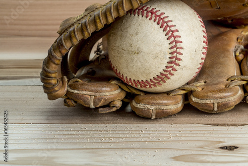 Old worn leather baseball glove and used ball on a wooden table background