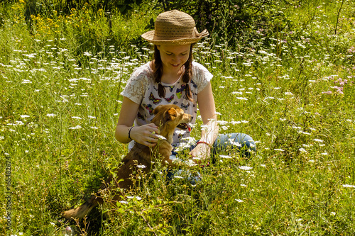 Smiling young girl with hair braids and hat with her pet dog in a field