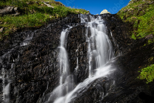 Kleiner Wasserfall im Gebirge unter blauem Himmel