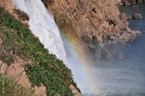 A part of Duden waterfall in Antalya  Lara  with a visible rainbow  Mediterranean sea  rocks and stones.