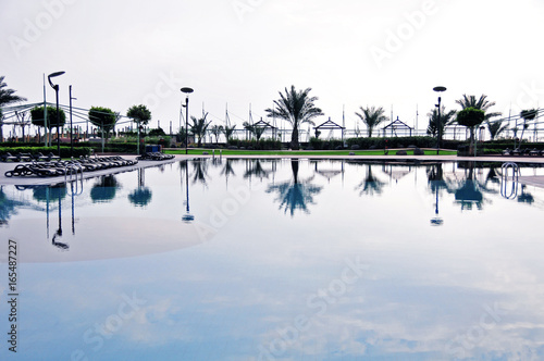 An outside swimming pool of Limak Lara Deluxe hotel, Antalya, Turkey, in the evening with a reflection of palms and other subjects. photo