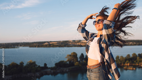 Beautiful young travel woman with flying hair. Tourist girl enjoying summer vacation at sunset.