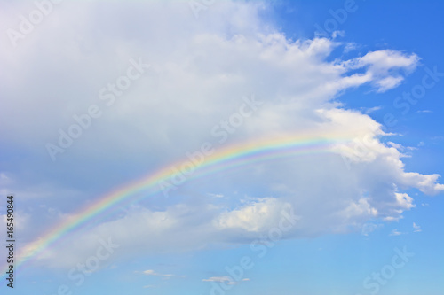 Rainbow under the white cloud on the azure sky.  Azure sky with a rainbow and a cloud. © IreneuszB