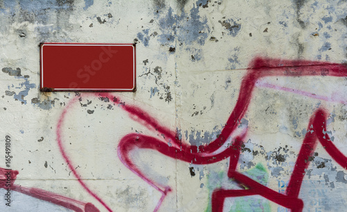 Red board on white flaked wall. Empty red signboard on grunge damaged urban wall with graffiti detail.