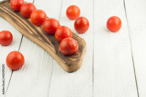 Fresh red and ripe tomatoes on rustic brown cutting board on old white wooden background