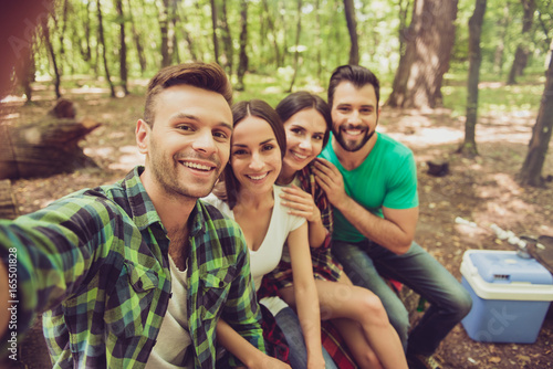 Close up of four happy friends tourists in the spring nice wood, embracing, posing for a selfie shot, that handsome blond guy is taking, sitting on a log © deagreez