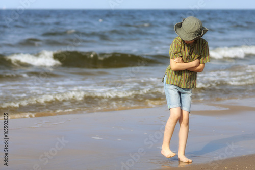 The boy stands on the sandy shore of the sea and freezes from the cold.