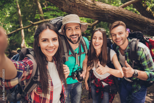 Close up of four cheerful  friends in the summer nice wood, embracing, posing for a selfie shot, that beautiful brunette lady is taking