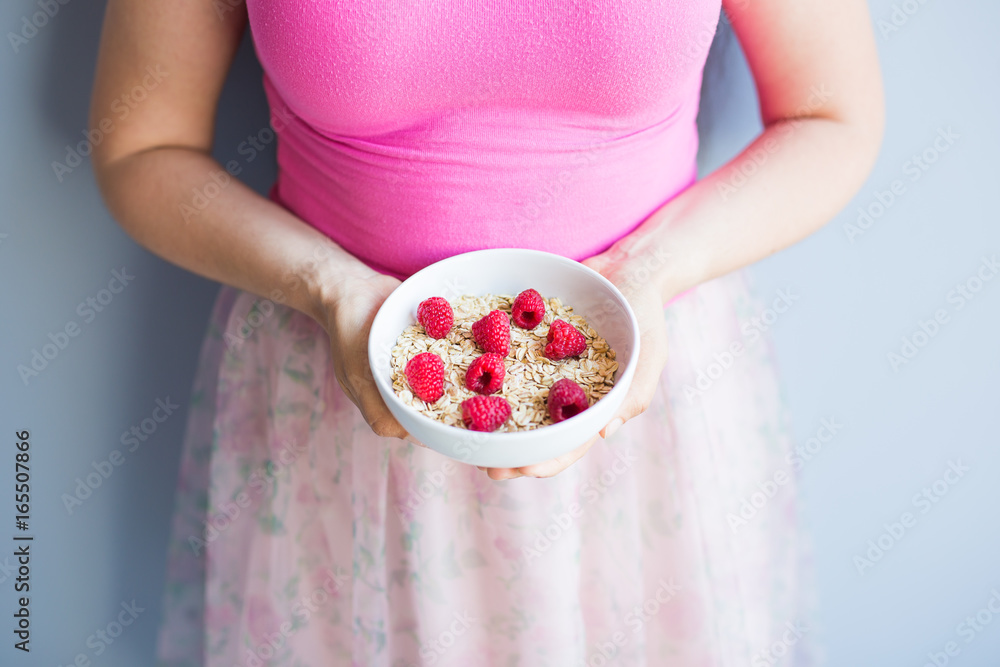 Woman's hands hold healthy and natural breakfast, oatmeal and raspberries in a bowl Woman's hands hold healthy and natural breakfast, oatmeal and raspberries in a bowl
