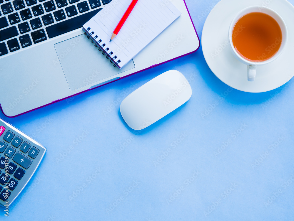 Top view of feminine desk workspace with office accessories including laptop, note book, red pencil, calculator and coffee on blue background. Top view of feminine desk workspace with office accessories including laptop, note book, red pencil, calculator and coffee on blue background.