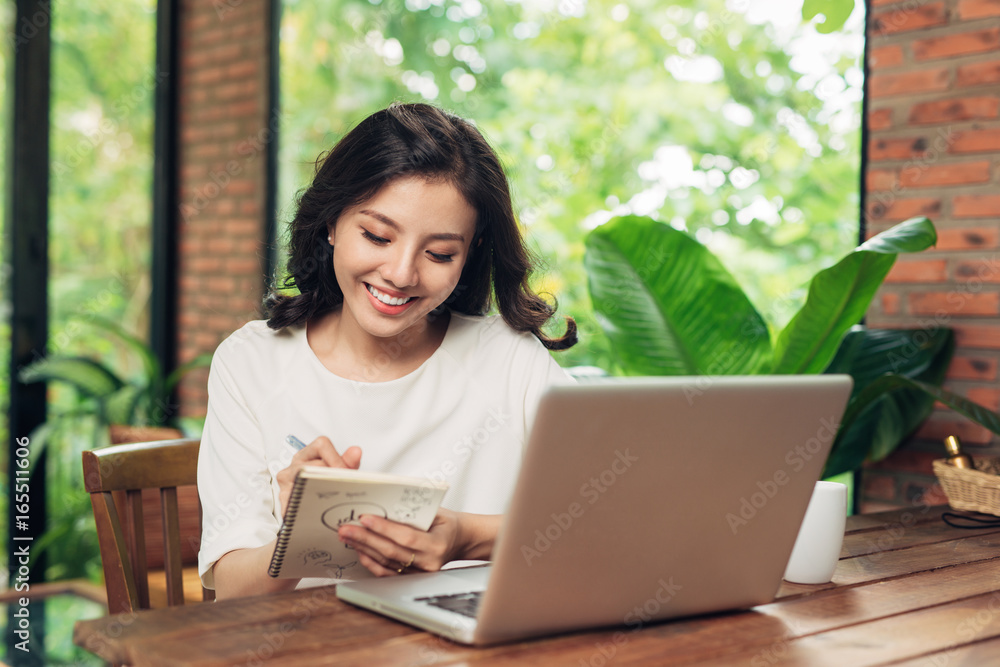 Beautiful young smiling woman working on laptop while sitting on bed at home near big window. Beautiful young smiling woman working on laptop while sitting on bed at home near big window.