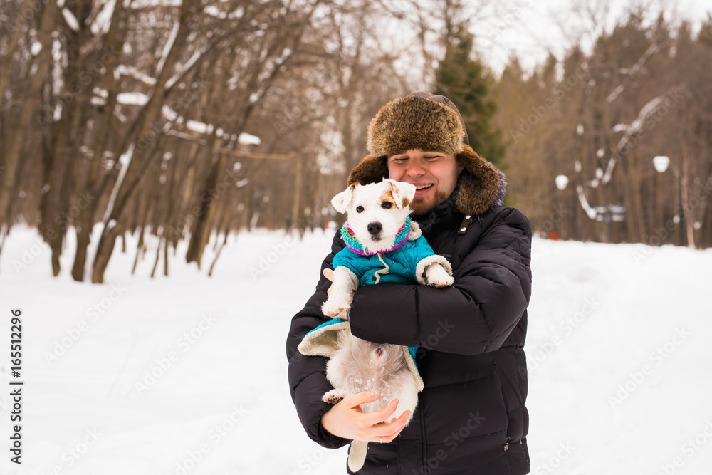 © satura_ - Pet owner, dog, and people concept - Young smiling caucasian man holding Jack Russell terrier outdoor in winter time.
