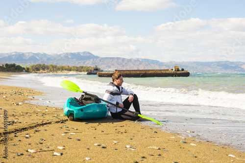 Man sitting on the beach with kayak. Traveling by sea. Leisure activities on the water.