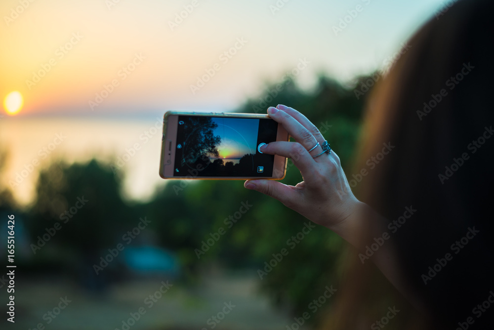 Young woman with smartphone taking a picture to the sunset
